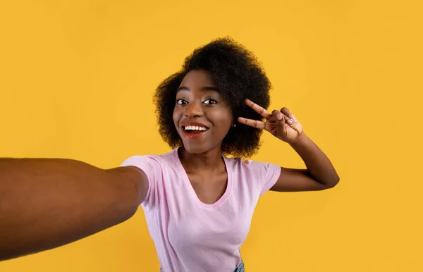 Pozitif Afro-Amerikalı kadın selfie çekiyor ve barış jesti gösteriyor, sarı arka planda kameraya gülümsüyor. — Stok fotoğraf