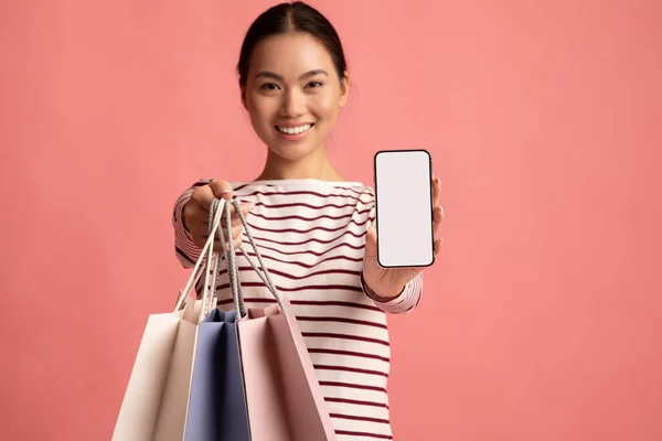 App di shopping online. Donna asiatica in possesso di borse che mostrano smartphone con schermo bianco — Foto Stock