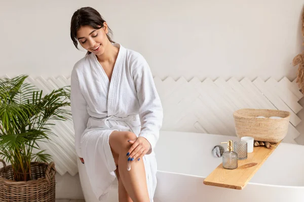Cuerpo hidratante de la mujer con la loción sentada en la bañera en el baño —  Fotos de Stock