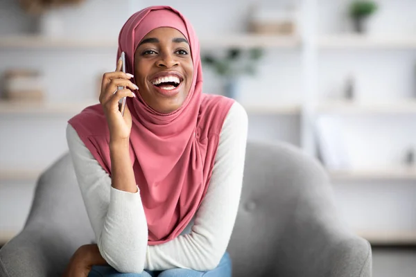 Vidám fekete muzulmán hölgy hidzsábban, aki otthon mobilon beszél., — Stock Fotó