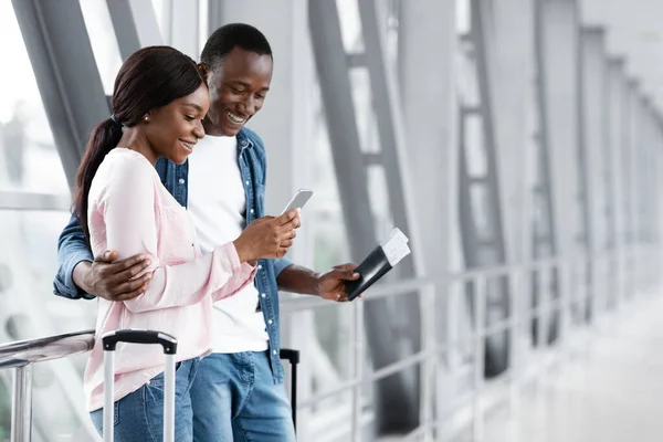 Щаслива афроамериканська пара, використовуючи смартфон в терміналі аеропорту, Бронювання готелю онлайн — стокове фото