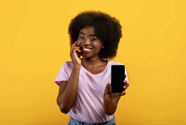 Pretty african american bushy woman showing smartphone with empty screen, advertising new app on yellow background — Stock Photo, Image