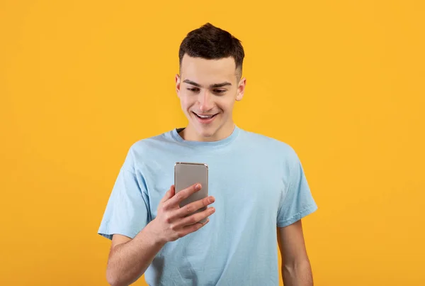 Pemuda ceria menggunakan telepon genggam, mengobrol online, mengadakan pertemuan bisnis atau webinar dengan latar belakang oranye — Stok Foto