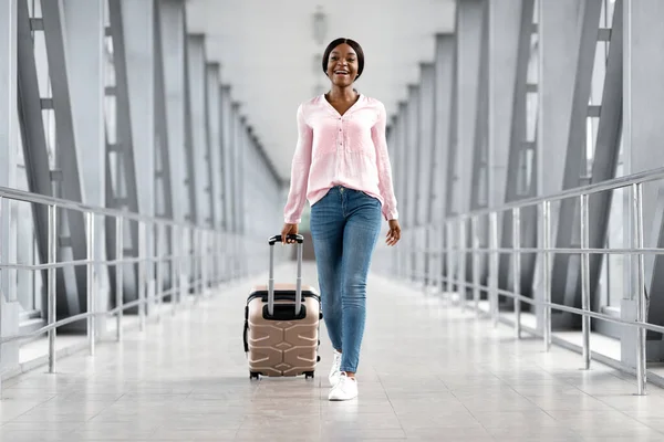 Letecká doprava. Šťastný africký Američan žena chůze v letištním terminálu s kufrem — Stock fotografie