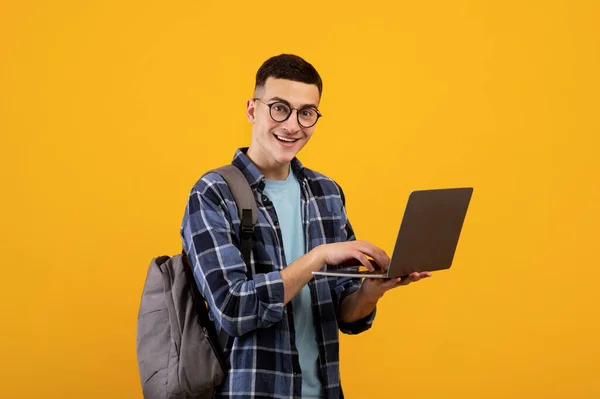 Inteligente joven estudiante con mochila usando ordenador portátil PC en fondo de estudio naranja — Foto de Stock