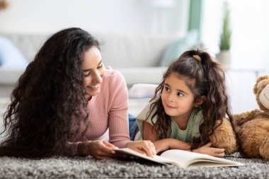 Sevgi dolu genç anne, küçük tatlı kızına evde kitap okuyor.