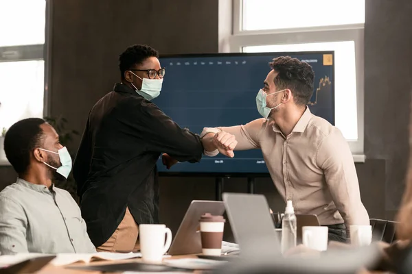 Diverse workers wearing face masks greeting and bumping elbows — Stock Photo, Image