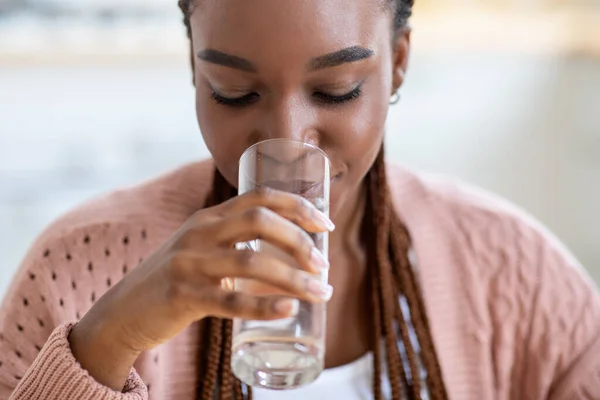 Orzeźwiający drink. Piękna młoda czarna pani wody pitnej ze szkła w domu — Zdjęcie stockowe