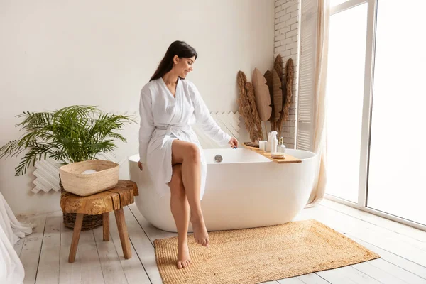 Vrouw voorbereiding bad toevoegen zout zitten op bad in de badkamer — Stockfoto