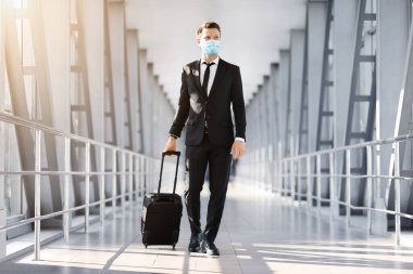 Yüzü maskeli zengin girişimci modern havaalanından geçiyor.