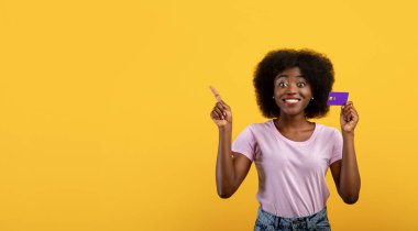 Reklam konsepti. Kredi kartı tutan Afrikalı Amerikalı kadın ve sarı arka plandaki boş yeri işaret ediyor.