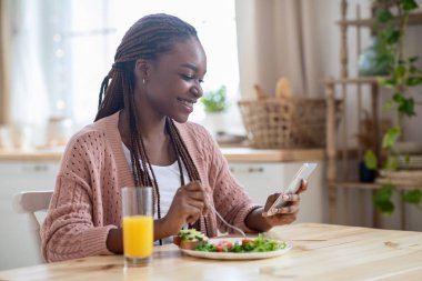 Kahvaltı yaparken Sosyal ağları Akıllı Telefona Kaydıran Mutlu Genç Zenci Kadın
