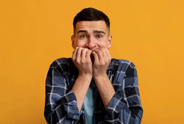 Jeune homme caucasien se sentant effrayé, se mordant les ongles en panique sur fond de studio orange. Émotions humaines négatives — Photo