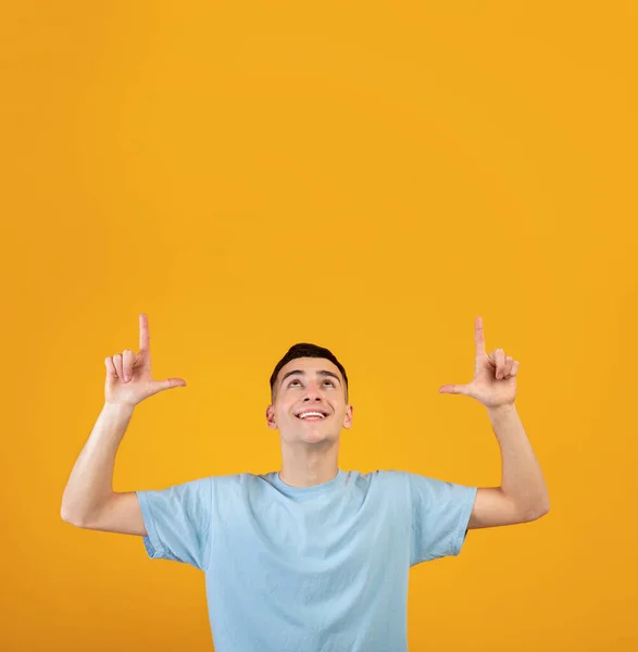 Joven alegre apuntando hacia arriba en el espacio en blanco para su anuncio en fondo de estudio naranja. Venta o descuento — Foto de Stock