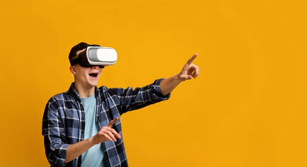 Cool young guy in virtual reality headset controlling cyber environment, pushing invisible button on virtual screen — Stock Photo, Image