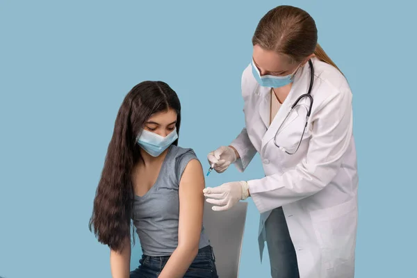 Concepto de inmunización Covid-19. Adolescente siendo vacunada contra coronavirus en el fondo azul del estudio — Foto de Stock