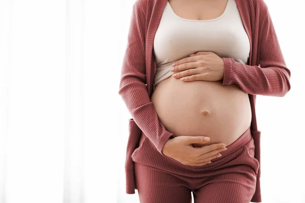 Обрезанный снимок беременной женщины, обнимающей свой обнажённый живот, крупным планом — стоковое фото