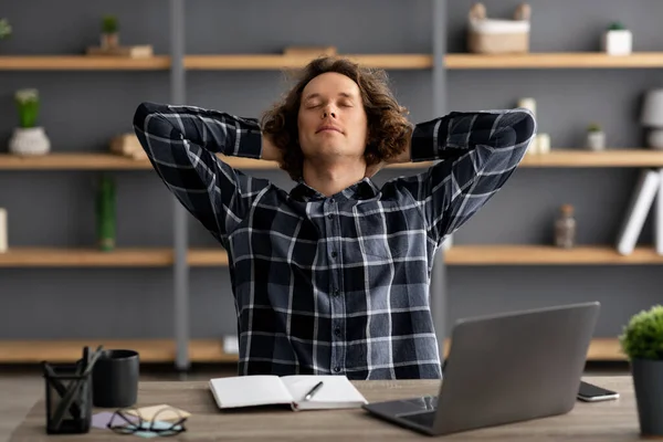 Cara no laptop descansando segurando as mãos atrás da cabeça no local de trabalho — Fotografia de Stock