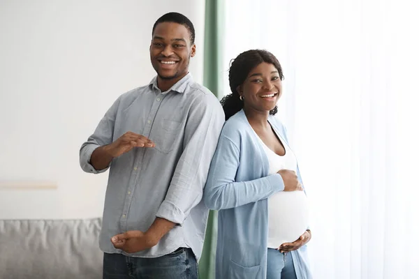 Amoroso homem negro imitando sua esposa grávida e sorrindo — Fotografia de Stock