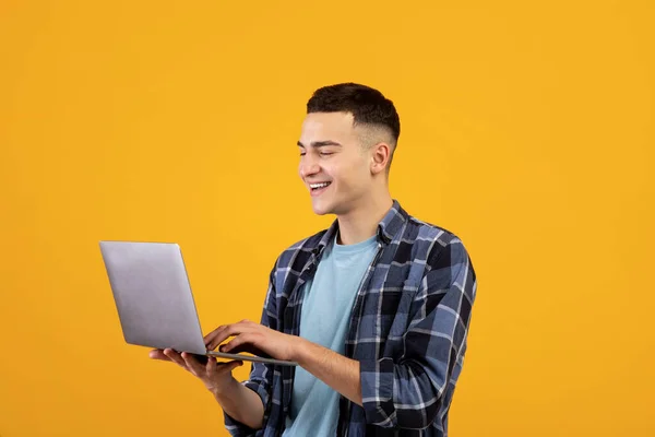 Joven feliz mirando la pantalla del ordenador portátil con sonrisa, viendo contenido web interesante en fondo de estudio naranja — Foto de Stock