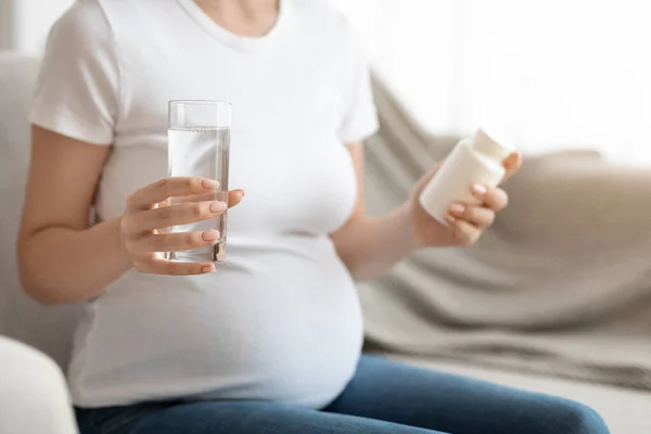 Kobieta w ciąży trzyma słoik z witaminami prenatalnymi i szklanką wody, upraw — Zdjęcie stockowe