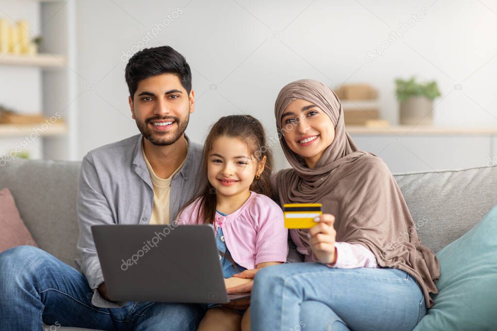 Online shopping concept. Happy muslim family using laptop computer and credit card, purchasing goods in internet