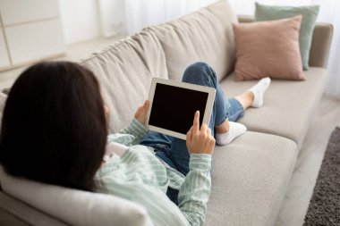 Tablet bilgisayarlı tanınmayan Hintli kadın rahat koltukta oturuyor ve internetten tasarım için çalışıyor.