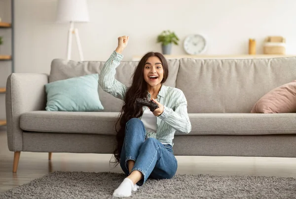 Femme indienne avec joystick assis sur le sol à la maison, faire un geste OUI, gagner un jeu vidéo, célébrer sa victoire — Photo