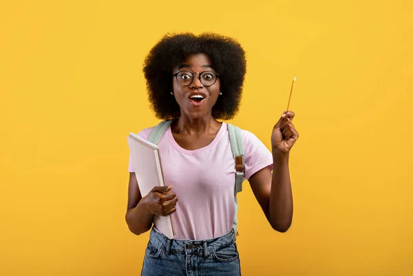 Bir fikrim var. Yaratıcı siyah kız öğrenci kalem kaldırıyor ve sarı stüdyo arka planında Eureka diye bağırıyor. — Stok fotoğraf