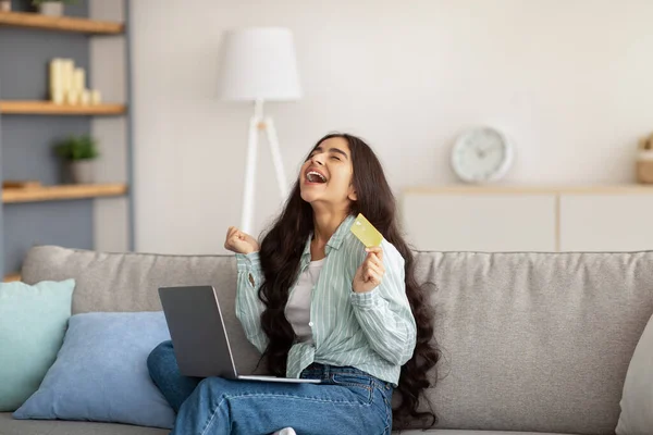 Excited Indian lady with laptop and credit card gesturing YES, happy over enormous discount in online store at home — Φωτογραφία Αρχείου