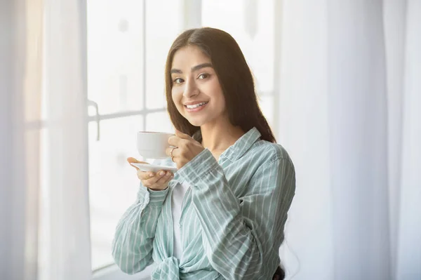 Lovely young Indian woman having coffee break in front of window at home — Stockfoto