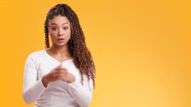 Afro-Amerikalı genç bayan şoke olmuş hissediyor, ağzını şaşkınlıkla kapatıyor, turuncu stüdyo arka planında boşluk var.