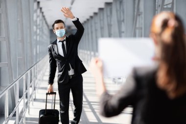 Businessman in face mask waving to assistance, meeting in airport