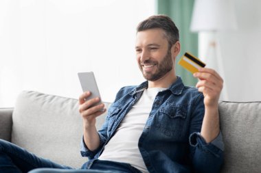 Positive man with smartphone holding credit card