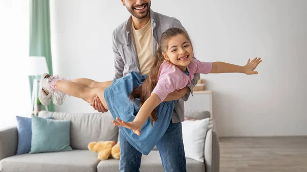 Family games. Happy young father carrying little daughter like plane, holding girl on hands and playing at home — Stock Fotó