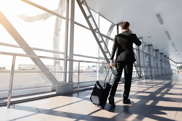 Businessman in suit walking by airport with suitcase, back view — ストック写真