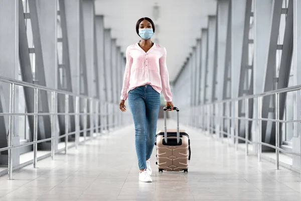 Pandemic Travel Concept. Young African Woman Wearing Medical Mask Walking In Airport