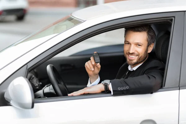 Cheerful businessman sitting in car, showing key — стоковое фото