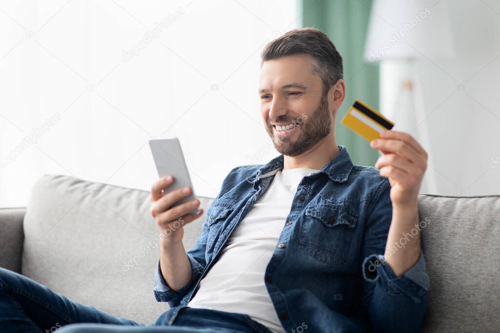 Positive man with smartphone holding credit card