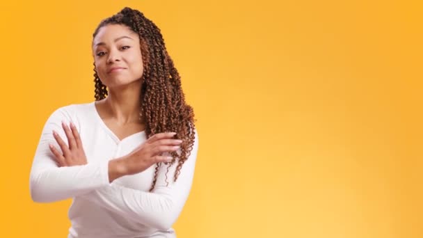 Young confident african american woman looking at camera with folded arms, orange studio background with free space — Stock Video