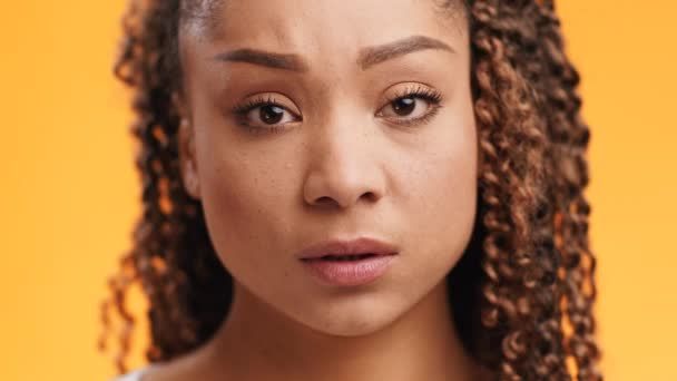 Cute young african american woman feeling upset, looking sadly at camera, close up portrait over orange background — Stock Video