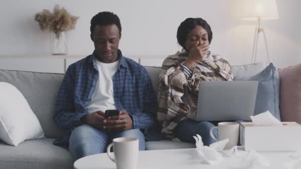 Jovem casal afro-americano sentado em casa juntos, mulher doente trabalhando no laptop e espirros, cara franzina — Vídeo de Stock