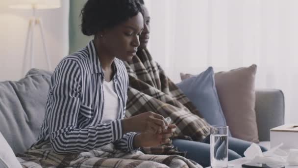 Młoda Afroamerykanka wkłada białą rozpuszczalną tabletkę do szklanki wody i podaje lek swojemu choremu chłopakowi. — Wideo stockowe