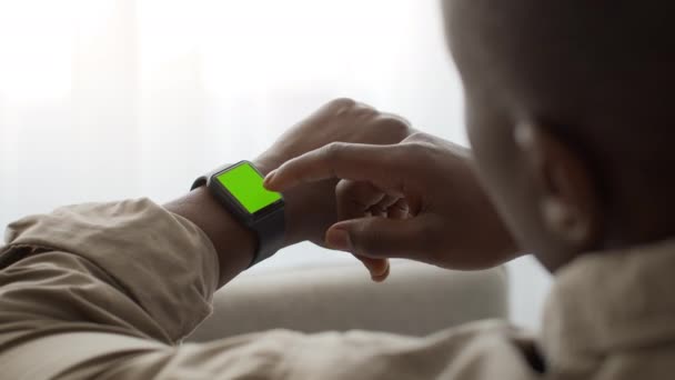 Afrikanischer Mann scrollt grünen Chroma-Keyscreen der Smartwatch, liest Nachricht oder überprüft seinen Gesundheitszustand — Stockvideo