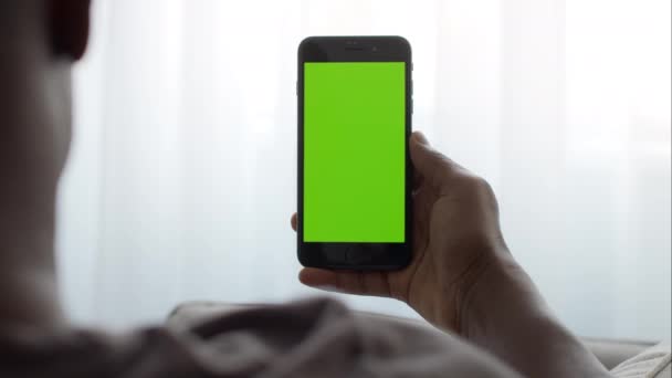 Vista posterior del irreconocible hombre afroamericano sosteniendo un teléfono inteligente moderno con pantalla clave de croma verde — Vídeos de Stock