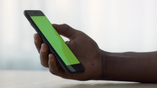 Hombre negro irreconocible sosteniendo teléfono inteligente con pantalla de clave de croma verde y viendo videos, espacio vacío para maqueta — Vídeos de Stock