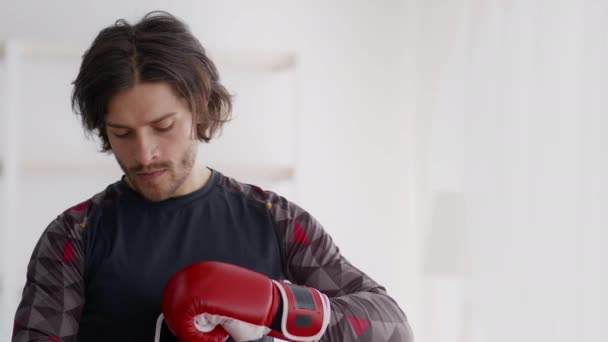 Jonge actieve man het aantrekken van rode bokshandschoenen, voor te bereiden om te beginnen met zelfverdediging workout, stoten vuisten, tracking schot — Stockvideo