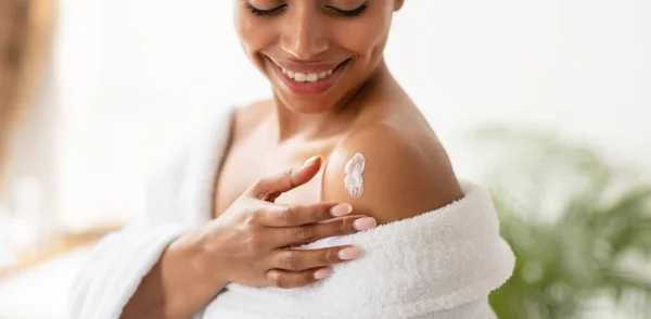 Mujer africana aplicando loción en los hombros hidratando la piel en el baño — Foto de Stock