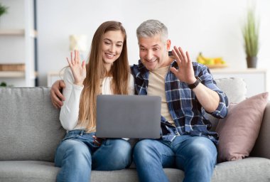 Neşeli evli çift cep telefonuyla arkadaşlarıyla görüntülü konuşma yapıyor, webcam 'e el sallıyor, kapalı alanda.