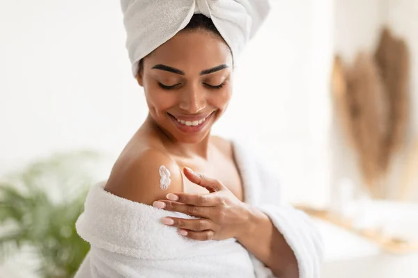 Senhora preta aplicando creme nos ombros hidratando a pele no banheiro — Fotografia de Stock